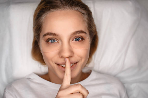 istock Cheerful nice young woman lying on white couch. She look straight on camera and keep finger on mouth. Hush. Silence. 1131134253