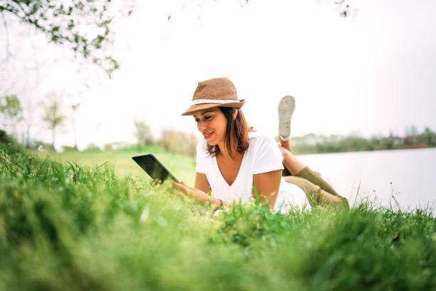 Young smiling woman laying on grass and using tablet.