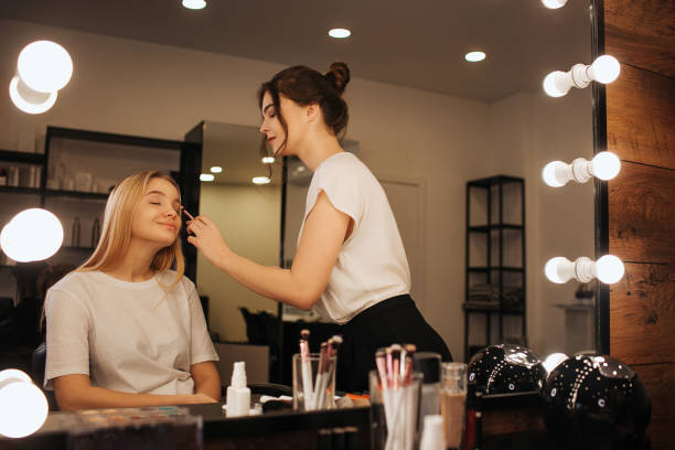istock Young make up artist put make up of young woman's face. She put eyeshadows using brush. Young blonde model sit calm in chair in beauty room. 1131138748