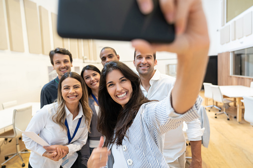 Portrait of a happy group of business people taking a selfie at a creative office using a cell phone - lifestyle concepts