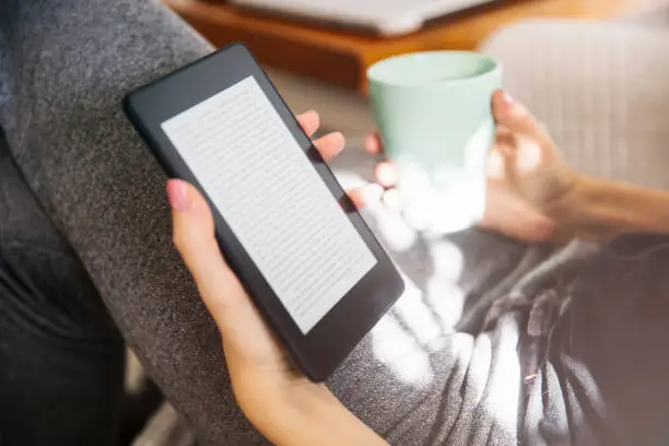 Young woman drinking coffee and using an ebook reader in the sofa