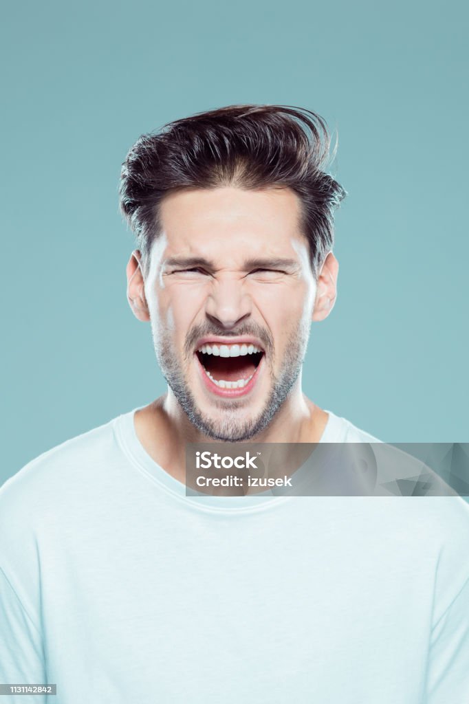 Angry young man screaming Close up portrait of angry young man screaming against gray background People Stock Photo