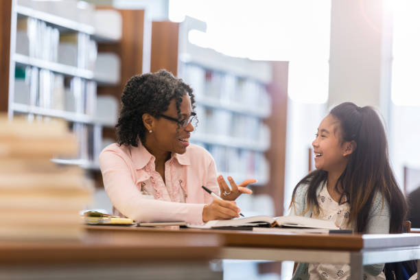 istock Little girl laughs with tutor in school library 1131145969