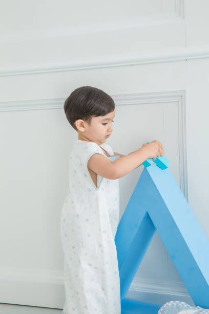 istock In the nursery's bedroom, next to a blue triangular cube, a cute little boy plays with pillows and blocks 1131147362