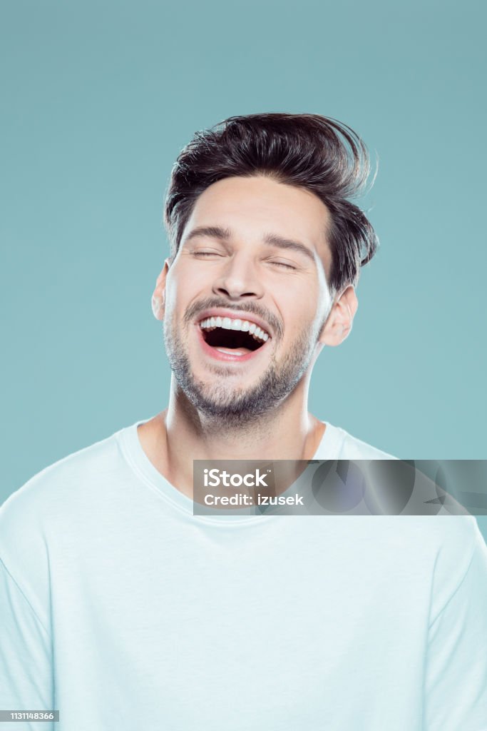 Close up of a laughing young man Close up portrait of young man laughing against gray background Men Stock Photo