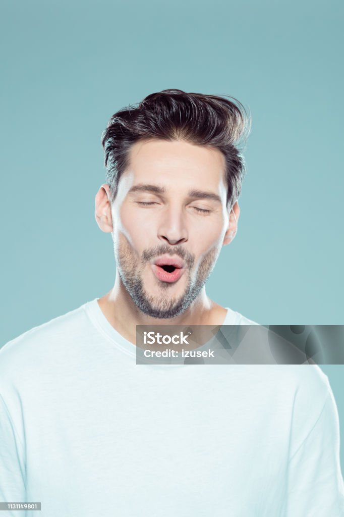 Young caucasian man looking happy Close up portrait of young caucasian man looking happy against gray background Eyes Closed Stock Photo