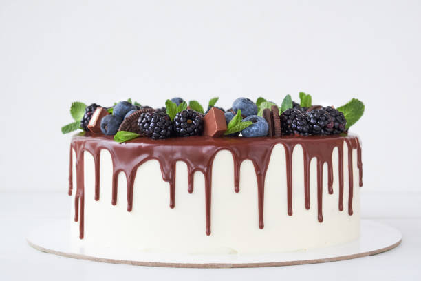istock Cake with chocolate, decorated with backberries, blueberries, mint leaves, chocolate bars and cookies on a white table. 1131153233