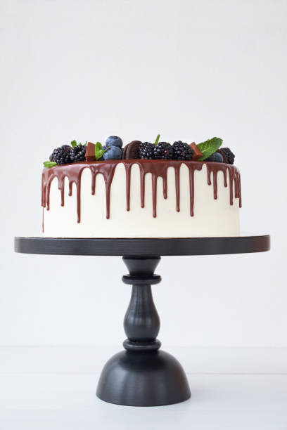 istock Cake with chocolate, decorated with backberries, blueberries, mint leaves, chocolate bars and cookies on a white table. 1131153236