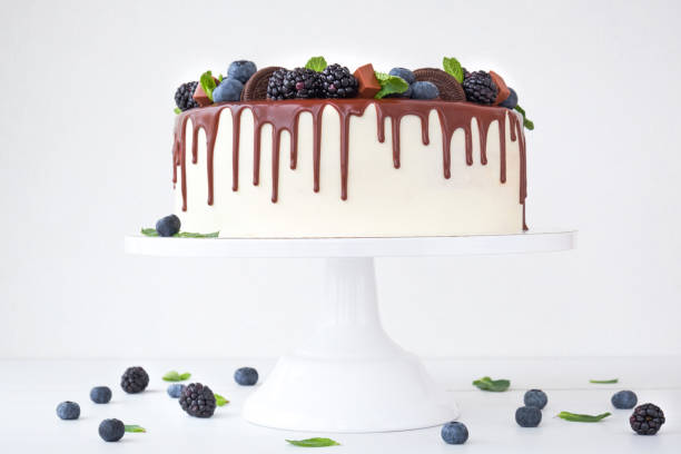 istock Birthday white cake with chocolate, decorated with black berries, mint leaves, chocolate bars and cookies on a white background. 1131153315