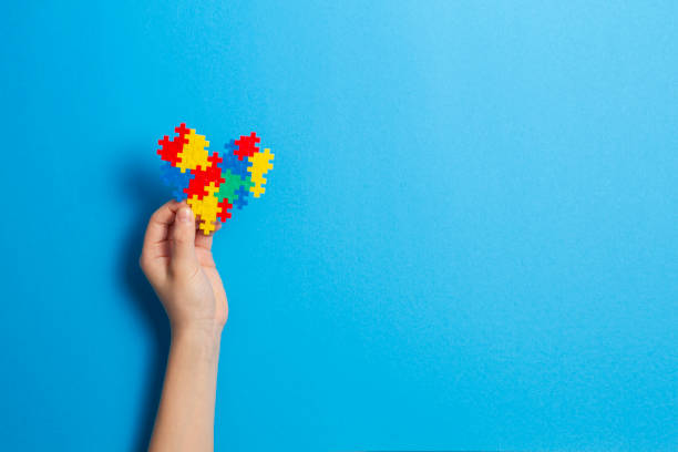 mano de niño sosteniendo el corazón colorido sobre fondo azul. concepto del día mundial del autismo - autism fotografías e imágenes de stock