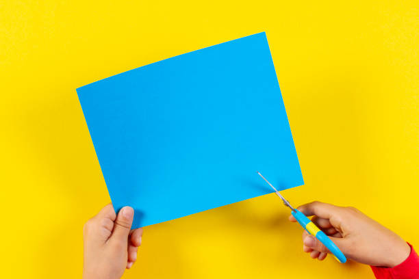 Kid's hands cutting colored paper with scissors, top view