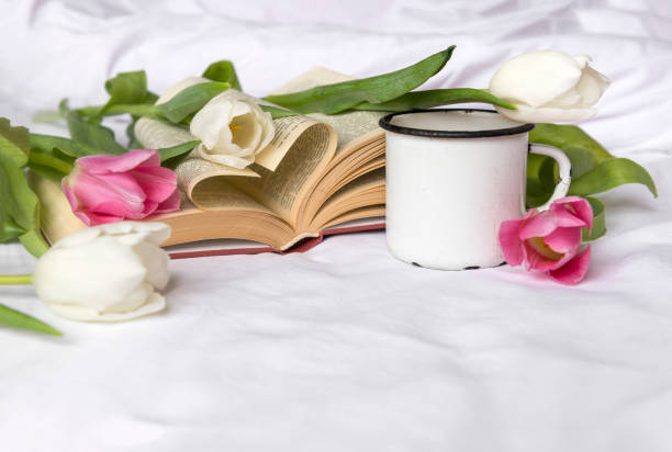 istock white and pink tulips, white mug on white sheet, open book 1131155673