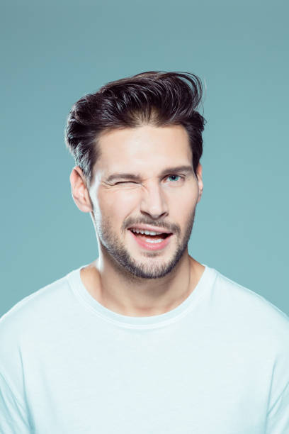 Handsome young man winking Close up portrait of handsome young man winking an eye against gray background young man wink stock pictures, royalty-free photos & images
