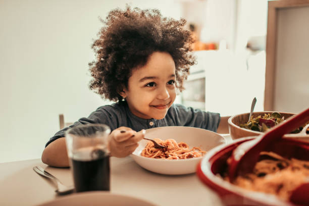 Family Lunch Beautiful girl sitting and eating spaghetti. kids eating noodles stock pictures, royalty-free photos & images
