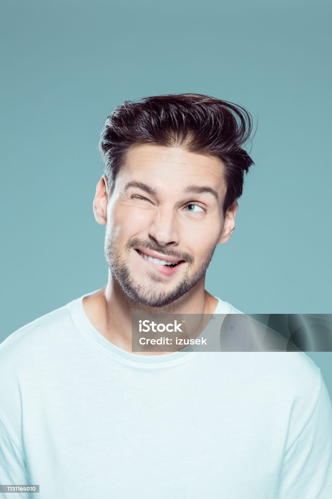 Close up of naughty young man Close up portrait of naughty young man winking a eye and biting his lips against gray background Men Stock Photo