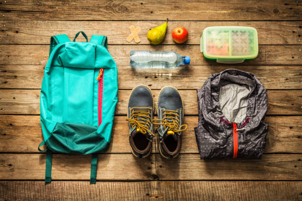 Traveling - packing (preparing) for adventure trip concept Traveling - packing (preparing) for adventure school trip concept. Backpack, boots, jacket, lunch box, water and fruits on wooden background captured from above (flat lay). packing stock pictures, royalty-free photos & images