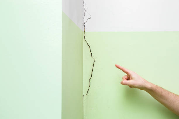 istock Man's hand finger pointing to cracked corner wall in house. Building problems and solutions concept. 1131171950
