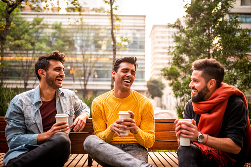 Low angle view on group of three male friends hanging out. They are having a coffee in the city.