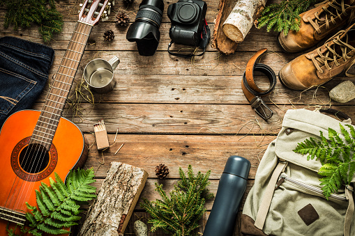 Camping or adventure trip scenery concept. Backpack, guitar, boots, belt, thermos and camera on wooden background captured from above (flat lay). Layout with free text (copy) space.