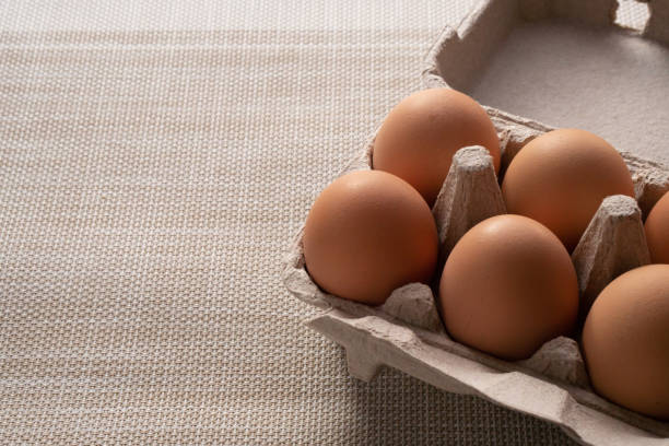 vista ravvicinata delle uova marroni fresche nella scatola per evitare che si rompa. è stato messo su una tela marrone per aspettare la cottura con un tagliere di legno posto accanto. - agriculture brown burlap cholesterol foto e immagini stock