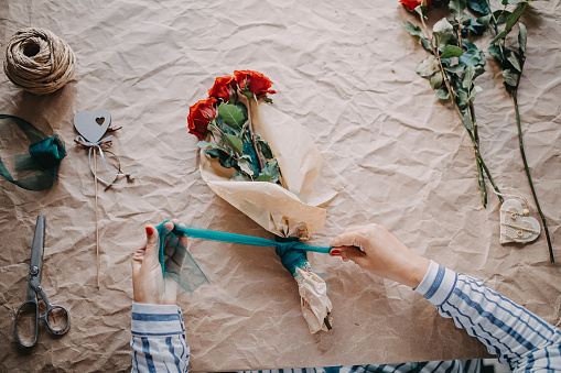 Womens hands wrap a bouquet of roses in paper
