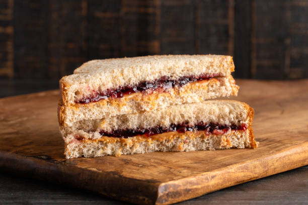 un sándwich de mantequilla de maní y jalea de uva en una tabla de corte de madera - peanut butter fotografías e imágenes de stock