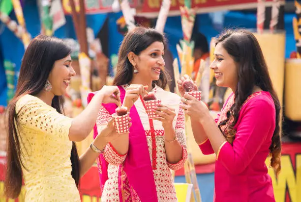 Indian women eating flavored ice gola dipped in syrup at street market