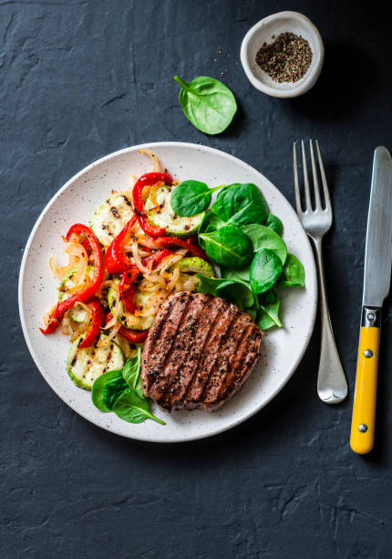 istock Beef steak with grilled  vegetables, sweet pepper, zucchini and fresh spinach on a dark background, top view. Delicious healthy balanced lunch 1131193680