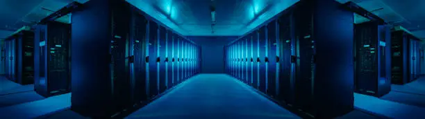 Photo of Wide-Angle Panorama Shot of a Working Data Center With Rows of Rack Servers. Blue Led Lights Blinking and Computers are Working. Dark Ambient Light.