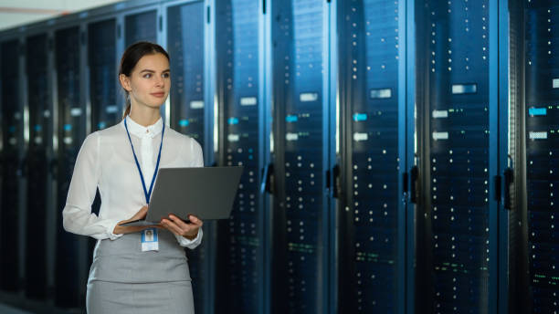 istock Beautiful Data Center Female IT Technician Walking Through Server Rack Corridor with a Laptop Computer. She is Visually Inspecting Working Server Cabinets. 1131198129