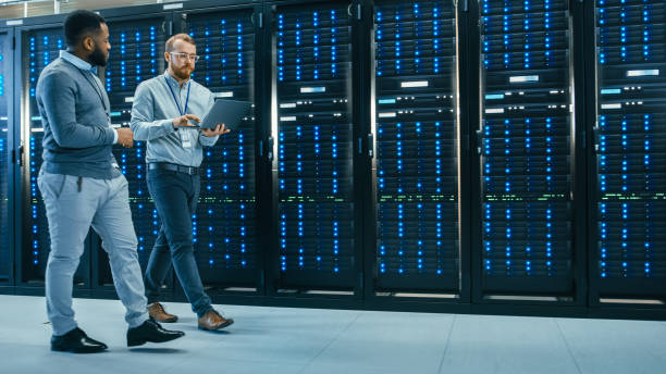 istock IT Technician with a Laptop Computer and Black Male Engineer Colleague are Talking in Data Center while Walking Next to Server Racks. Running Diagnostics or Doing Maintenance Work. 1131198258