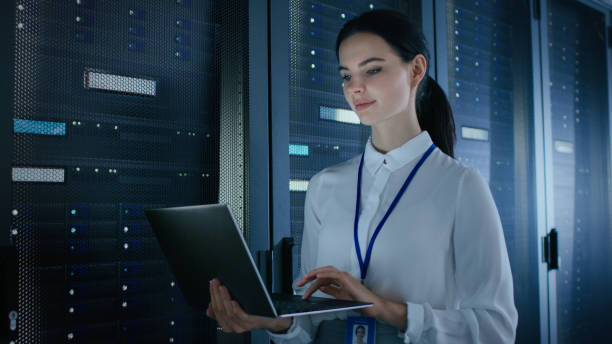 istock Confident and Beautiful Female IT Engineer is Working on Laptop in Data Center while Standing Before Server Rack. Running Diagnostics or Doing Maintenance Work. 1131198451