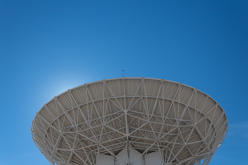 Very Large Array backlit radio astronomy observatory dish in clear sky, science technology space, horizontal aspect