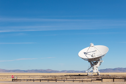 Very Large Array detail of radio antenna against a blue sky and distant mountains, listening to space, horizontal aspect