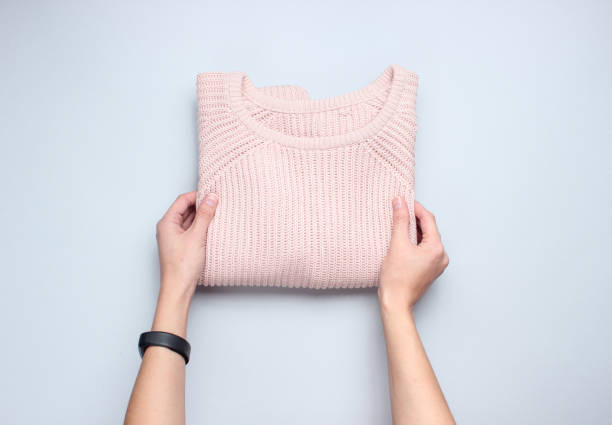 Hands fold knitted sweater on a gray background. Conceptual photo. Top view