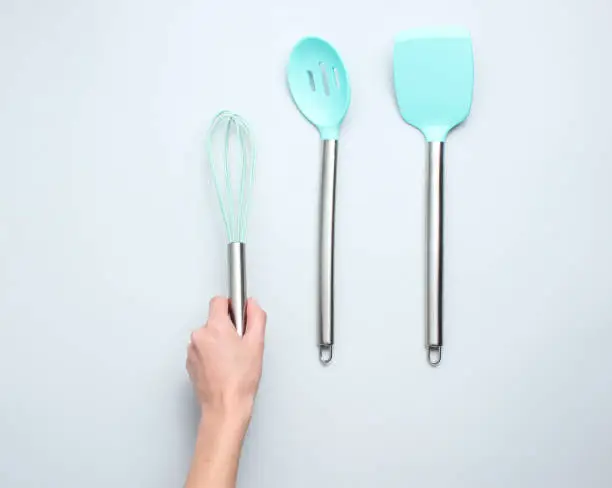 Hand holding silicone whisk for cooking with metal handle on a gray background. Top view."n