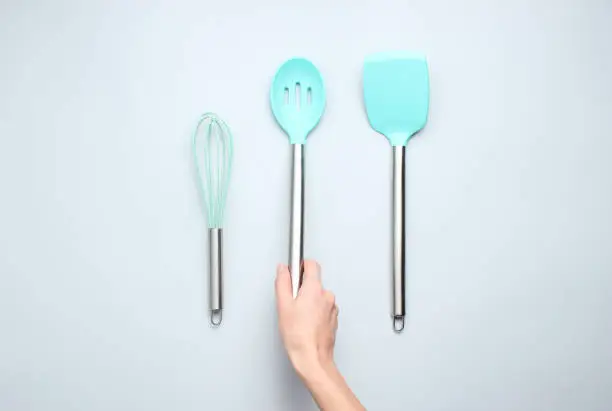 Hand holding silicone ladle for cooking with metal handle on a gray background. Top view.