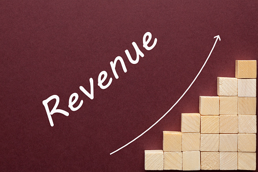 Revenue word on ascending arrow above wooden cubes. Business Concept.