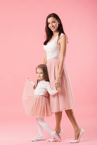 pretty, charming mother and smiling daughter on pink background, hugging, looking at camera, women's day. Mother's day
