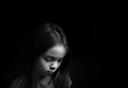 Low key picrure of a girl looking sad. High contrast picture in front of a black background.