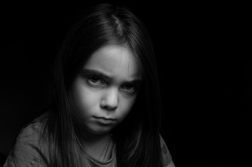 Low key picrure of a girl looking sad. High contrast picture in front of a black background.