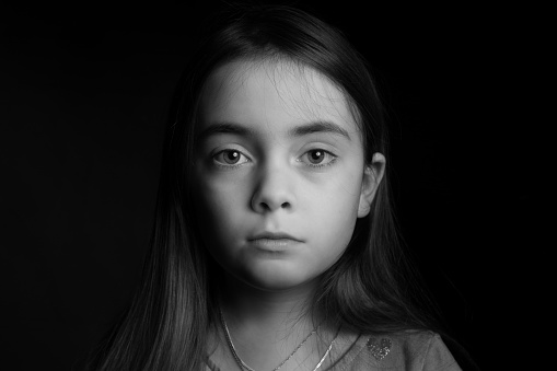 Frontal Portrait . Low key picrure of a girl looking sad straight in the camera .High contrast picture in front of a black background.