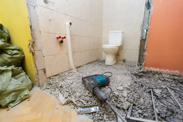 Toilet room or restroom with old toilet bowl and construction tool  - perforator  are in apartment that is under construction, remodeling, renovation, overhaul, extension, restoration and reconstruction. Concept of total home improvement or renovate