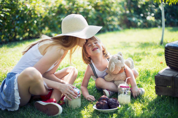 A young Eurasian girl relaxes in a patio chair with her little brother at her side as they eat pizza during the girl's casual backyard birthday party.