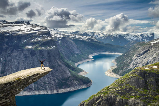 person, die am rande eines vorstehenden felsens über einem fjord in norwegen steht - mountain peak norway reflection sunlight stock-fotos und bilder