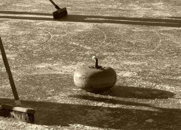 Curling stone with sweeper brooms close to house
