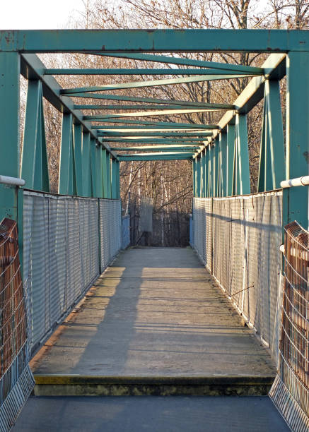 istock a perspective view along an green rusting metal pedestrian footbridge with rails and girders casting shadows in afternoon sunlight with trees in the background 1131237100