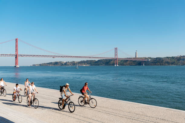 People ride their bicycles along the Maat Museum. Behind it is the bridge of April 25 and Christ the King. stock photo