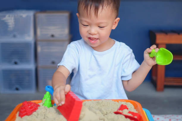 niedlich lächelnd asiatisch 2-3 jahre alt kleinkind spielen mit kinetischem sand in sandkasten zu hause/kindergarten/tagespflege - sandbox child human hand sand stock-fotos und bilder