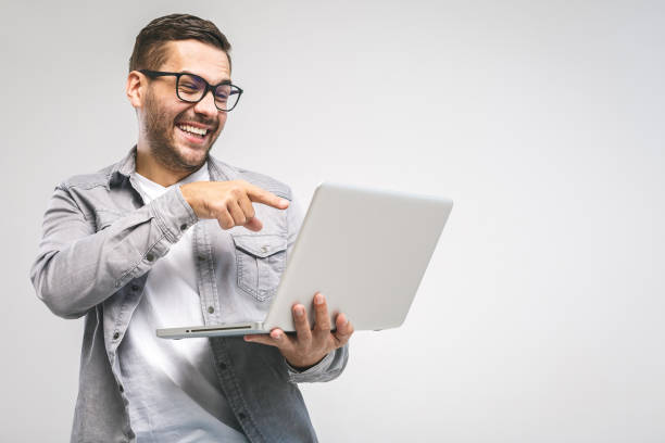 istock Funny young handsome man in shirt holding laptop and smiling while standing against white background. Have fun. 1131244971